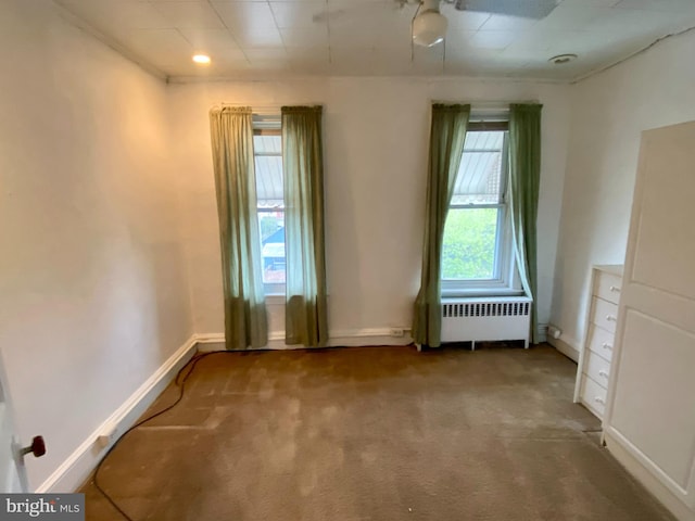 carpeted spare room featuring radiator and baseboards
