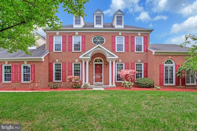 colonial-style house featuring brick siding, a front lawn, and roof with shingles