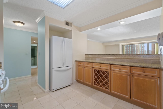 kitchen featuring freestanding refrigerator, ornamental molding, a textured ceiling, baseboards, and light tile patterned flooring