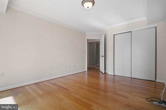 unfurnished bedroom with light wood finished floors, crown molding, baseboards, and a closet