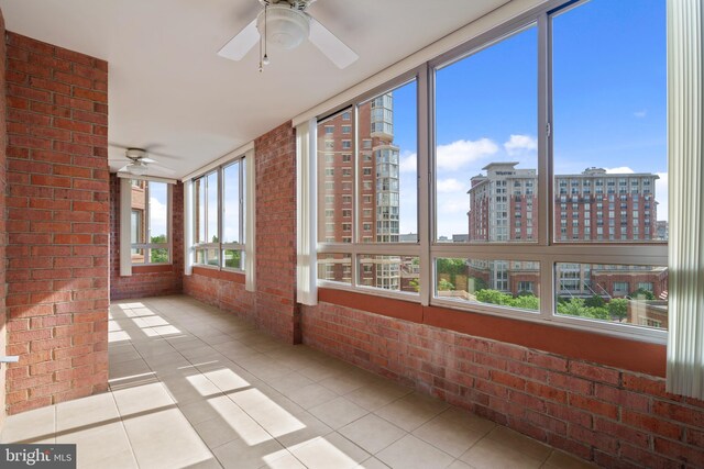 unfurnished sunroom featuring ceiling fan, brick wall, a view of city, and tile patterned flooring