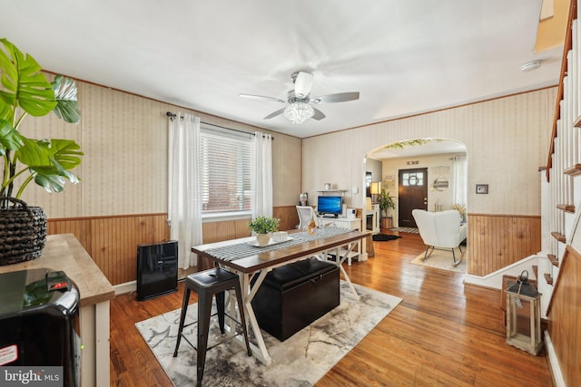 dining area featuring arched walkways, stairway, a wainscoted wall, and ceiling fan
