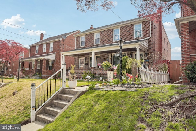 view of front of house with a porch, a chimney, fence, brick siding, and a front lawn