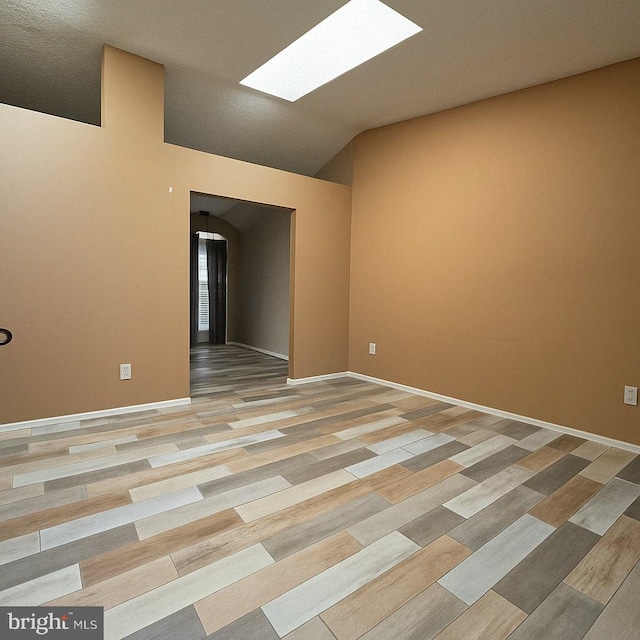 unfurnished room with baseboards, lofted ceiling with skylight, and light wood finished floors