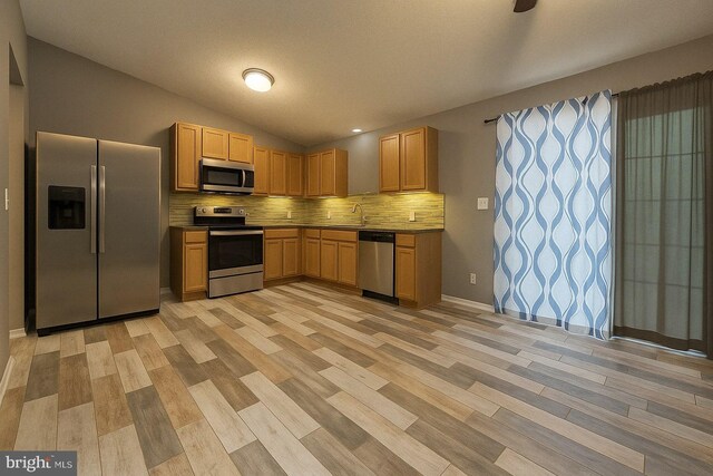 kitchen with stainless steel appliances, vaulted ceiling, baseboards, light wood-style floors, and decorative backsplash