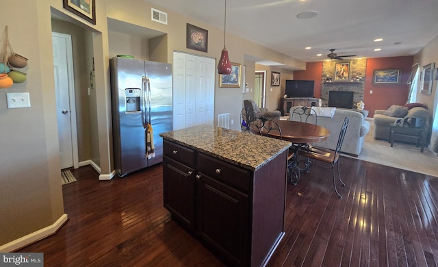 kitchen featuring a ceiling fan, a stone fireplace, visible vents, stainless steel refrigerator with ice dispenser, and dark wood-style flooring