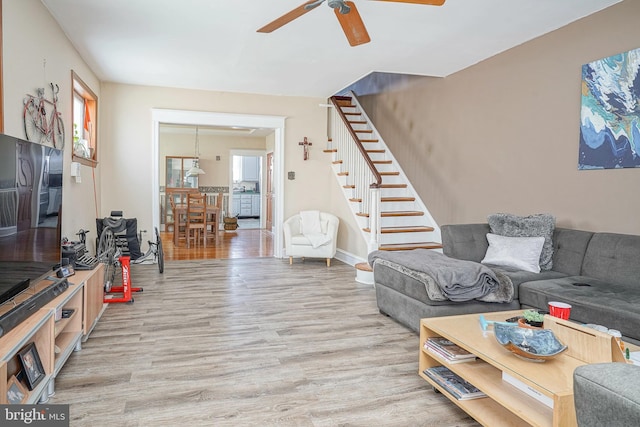 living room with stairway, baseboards, a ceiling fan, and light wood-type flooring