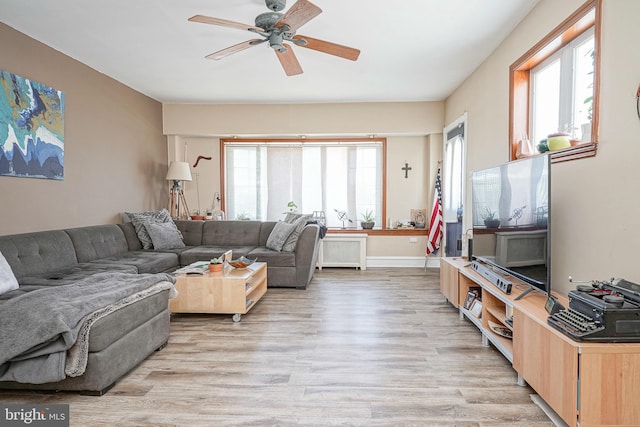 living room with radiator, baseboards, a ceiling fan, and light wood-type flooring