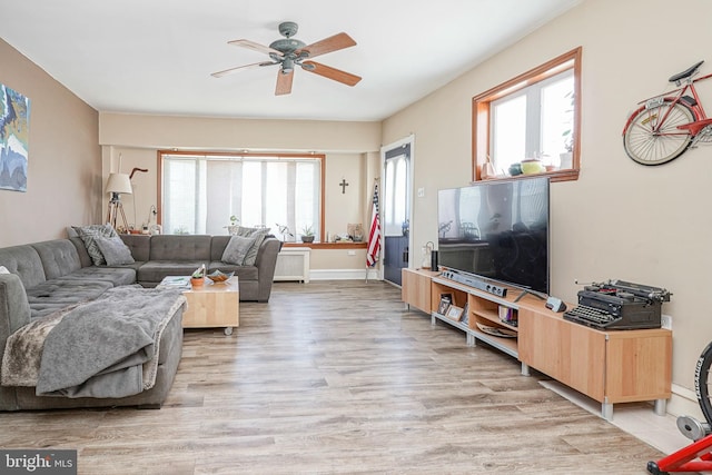 living room with ceiling fan, baseboards, and light wood finished floors
