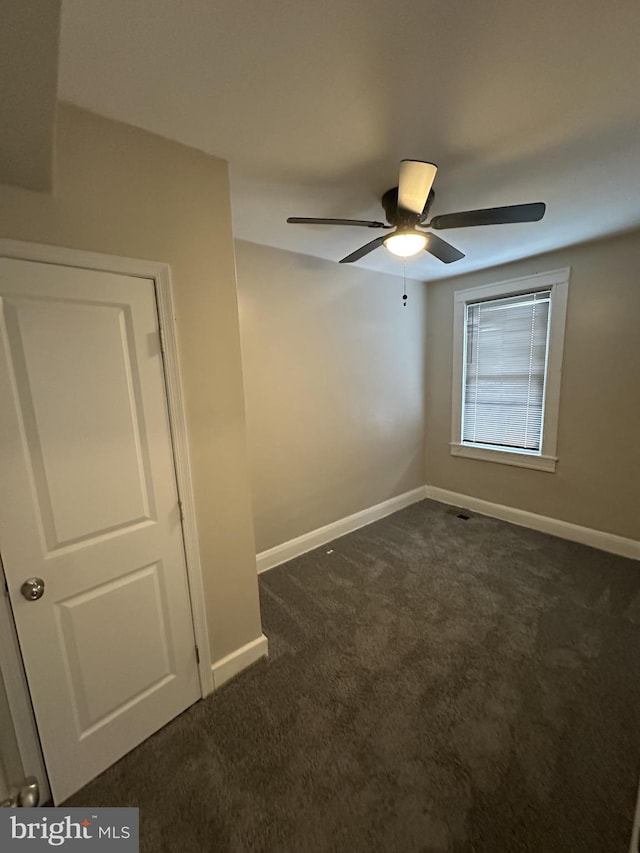 empty room with baseboards, a ceiling fan, and dark colored carpet