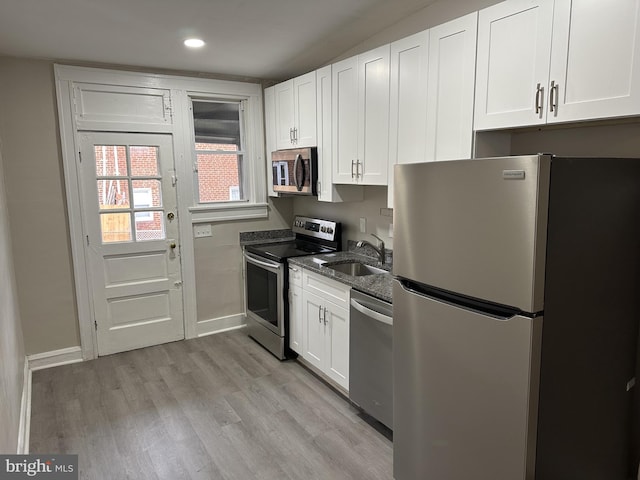 kitchen with a sink, stainless steel appliances, baseboards, white cabinetry, and light wood-type flooring