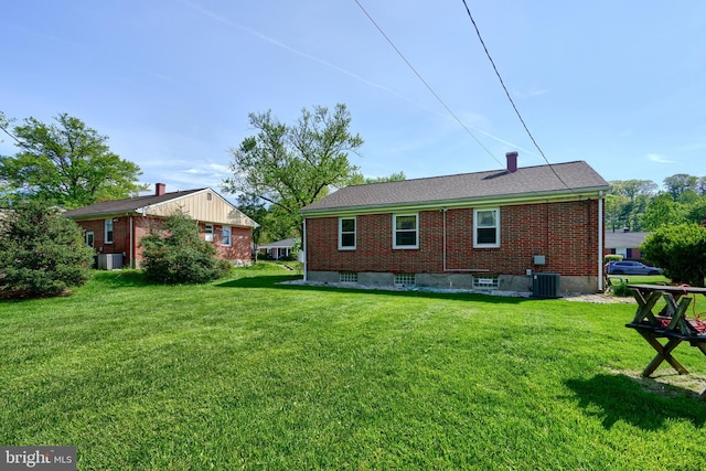 back of house featuring central air condition unit, brick siding, and a yard