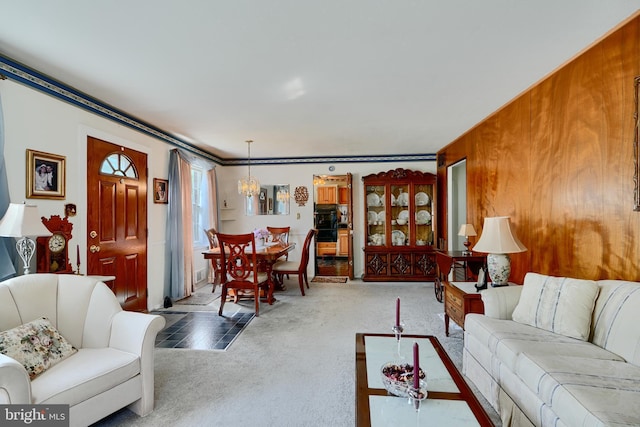 living room with wooden walls, ornamental molding, carpet, and an inviting chandelier