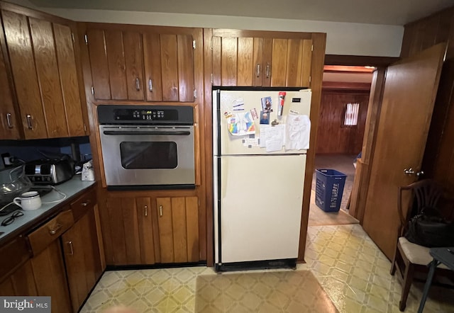 kitchen featuring stainless steel oven, freestanding refrigerator, light floors, and brown cabinets