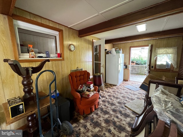 living area featuring beamed ceiling, wooden walls, and carpet floors
