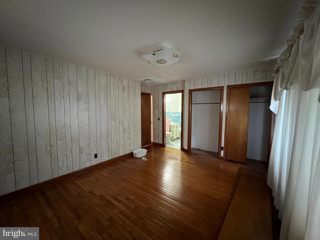 unfurnished bedroom featuring ensuite bath, wood finished floors, and multiple closets