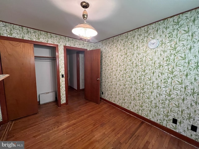 unfurnished bedroom featuring crown molding, wood finished floors, wallpapered walls, a closet, and baseboards