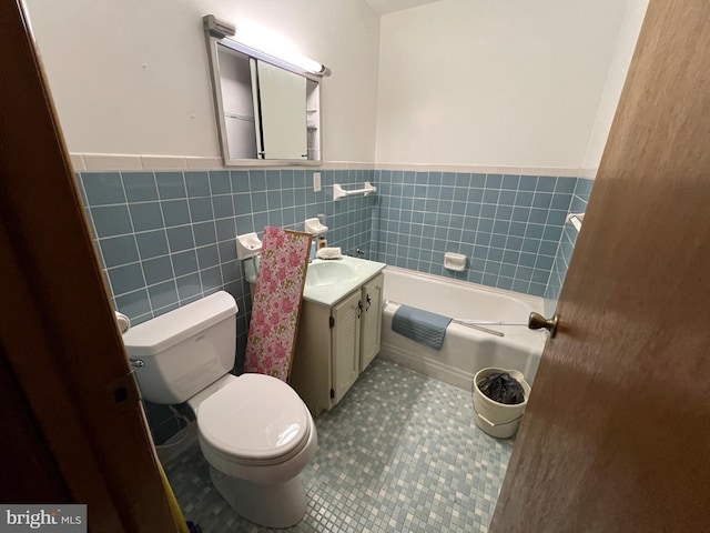 bathroom with a washtub, toilet, vanity, tile walls, and wainscoting