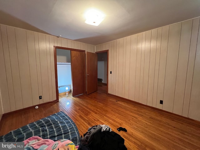 unfurnished bedroom with wood finished floors, wood walls, and baseboards