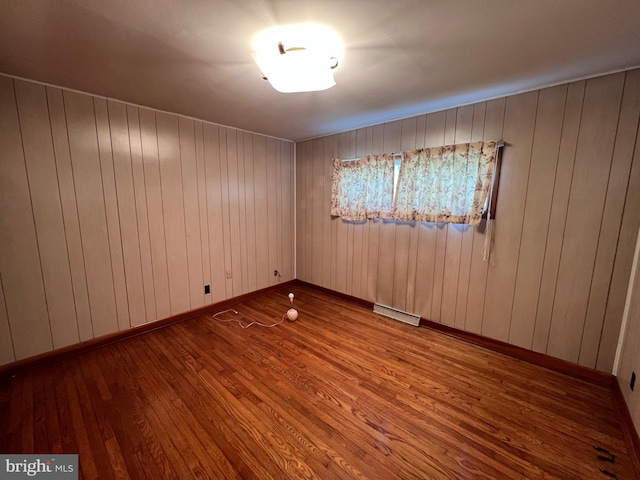 spare room with wood walls, baseboards, wood finished floors, and visible vents