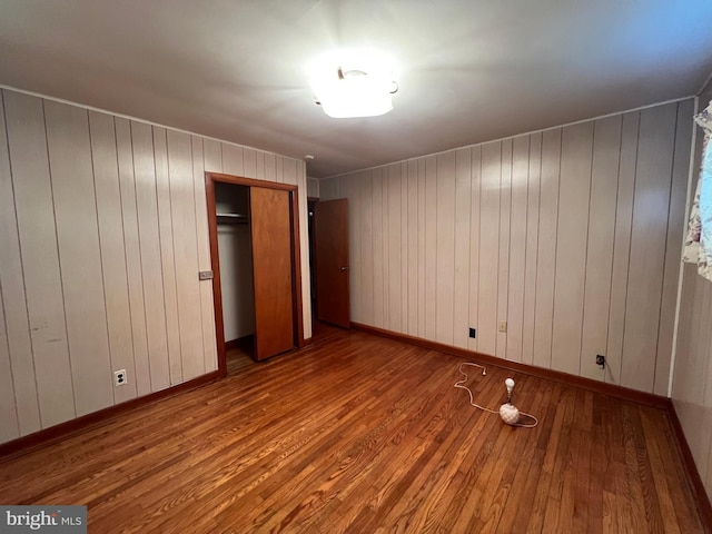unfurnished bedroom with wood finished floors, a closet, and wood walls