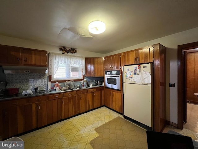 kitchen featuring oven, under cabinet range hood, light floors, a sink, and freestanding refrigerator
