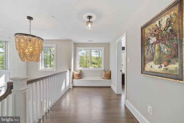 hall featuring baseboards, a chandelier, a healthy amount of sunlight, and wood finished floors