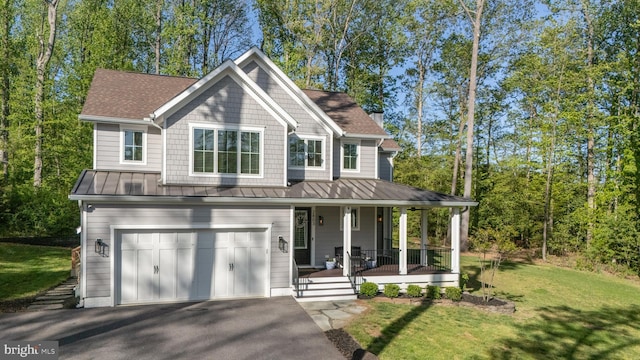 view of front of property featuring a front lawn, an attached garage, a standing seam roof, a porch, and driveway