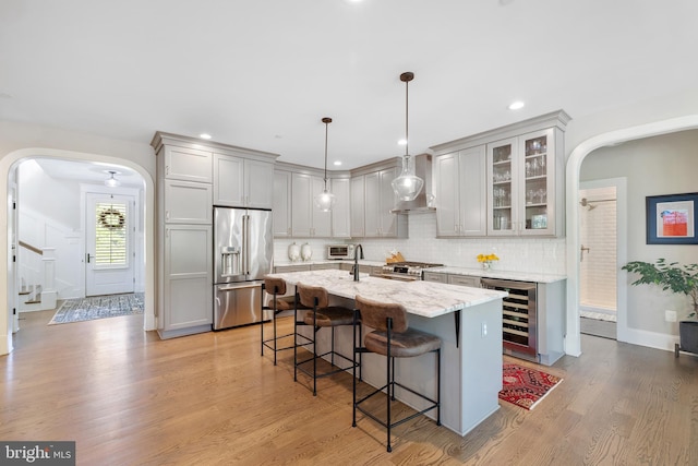 kitchen featuring wall chimney range hood, arched walkways, premium appliances, and beverage cooler