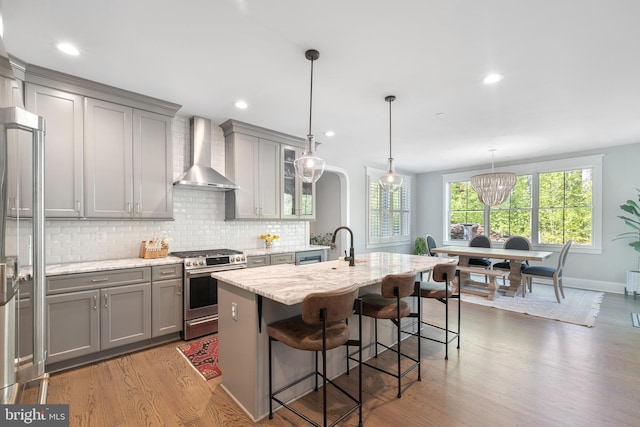 kitchen featuring wall chimney range hood, backsplash, stainless steel gas range oven, wood finished floors, and gray cabinetry