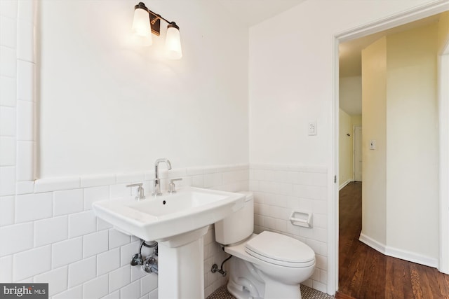 half bath featuring wainscoting, a sink, toilet, tile walls, and wood finished floors