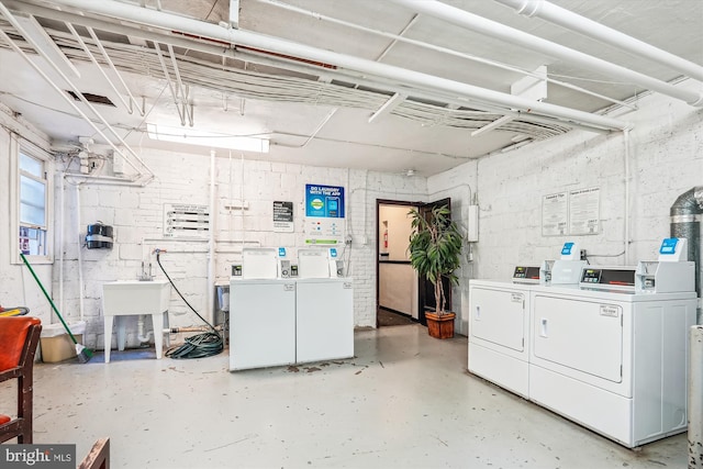 common laundry area featuring washing machine and clothes dryer, concrete block wall, and a sink