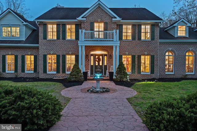 view of front of property featuring a front lawn, brick siding, and a balcony