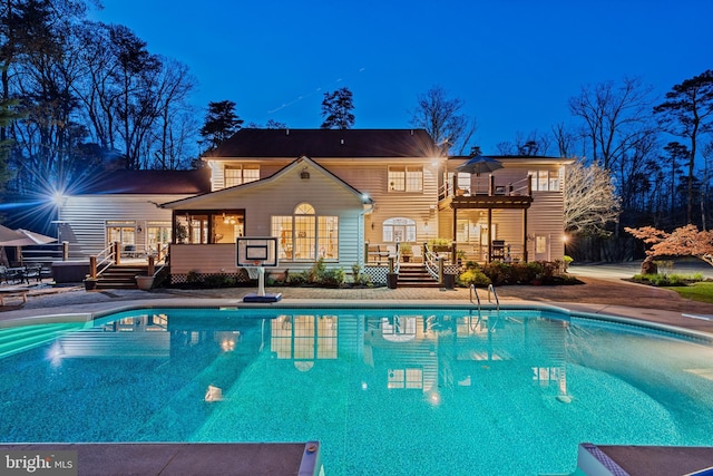 pool at night with a patio, an outdoor pool, and a wooden deck