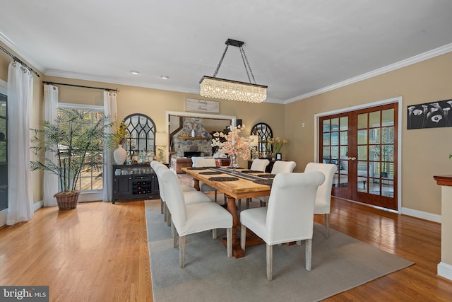 dining room with baseboards, a stone fireplace, crown molding, wood finished floors, and french doors