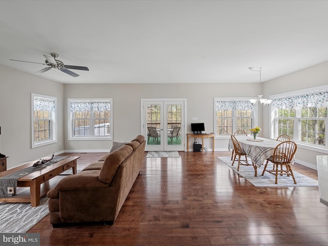 living area featuring a wealth of natural light, ceiling fan with notable chandelier, dark wood-style floors, and baseboards