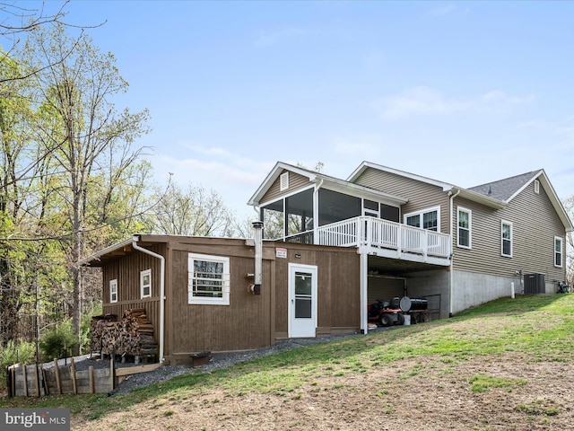rear view of house featuring central air condition unit, a wooden deck, a sunroom, and a yard