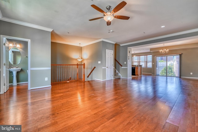 unfurnished living room with baseboards, ornamental molding, wood finished floors, and ceiling fan with notable chandelier
