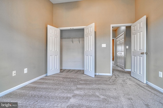unfurnished bedroom featuring baseboards, carpet, a closet, and a towering ceiling