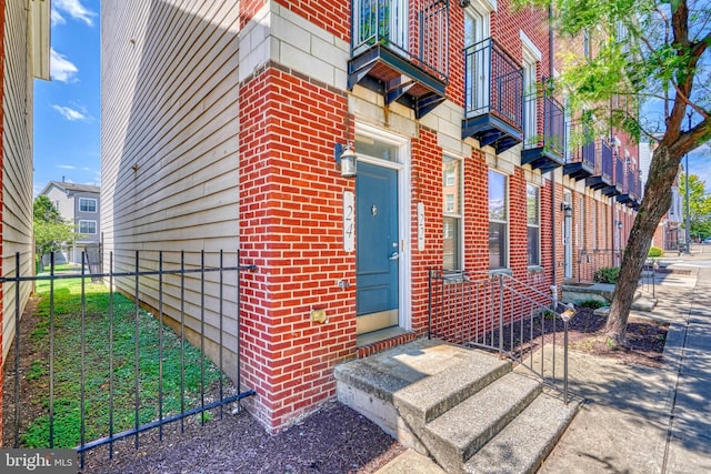 view of exterior entry with brick siding and fence