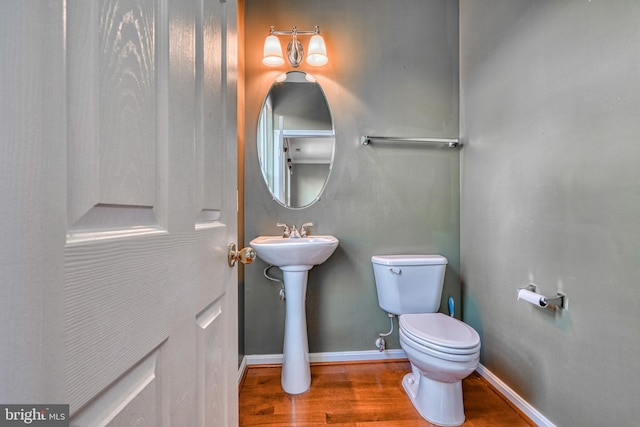 half bath with baseboards, a sink, wood finished floors, and toilet