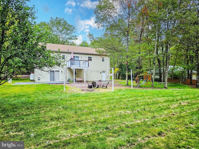 rear view of property with a playground, an outdoor fire pit, a lawn, and a deck