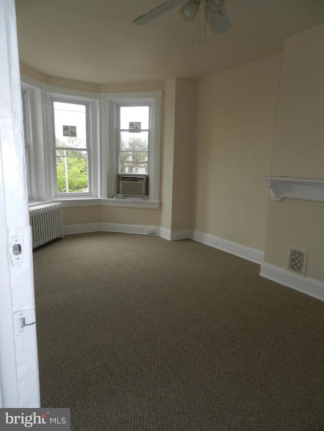 carpeted spare room featuring radiator, ceiling fan, cooling unit, visible vents, and baseboards