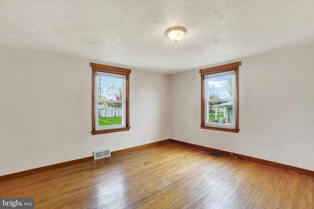 unfurnished room with visible vents, a wealth of natural light, hardwood / wood-style flooring, and baseboards