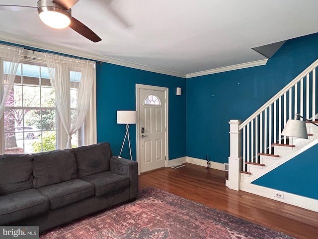 living area featuring stairway, wood finished floors, a ceiling fan, crown molding, and baseboards