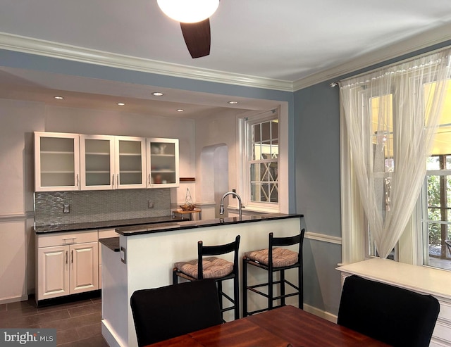kitchen featuring white cabinets, dark countertops, glass insert cabinets, a kitchen bar, and tasteful backsplash