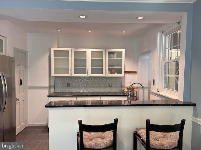 kitchen with freestanding refrigerator, a kitchen bar, white cabinetry, and a sink