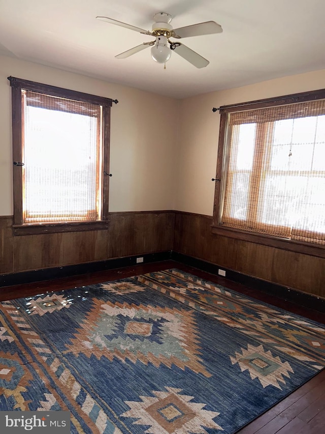 spare room with wainscoting, hardwood / wood-style flooring, a ceiling fan, and a healthy amount of sunlight