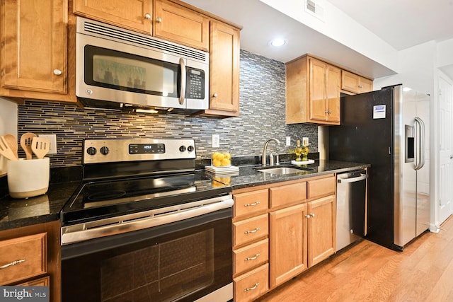 kitchen featuring visible vents, a sink, stainless steel appliances, light wood finished floors, and decorative backsplash