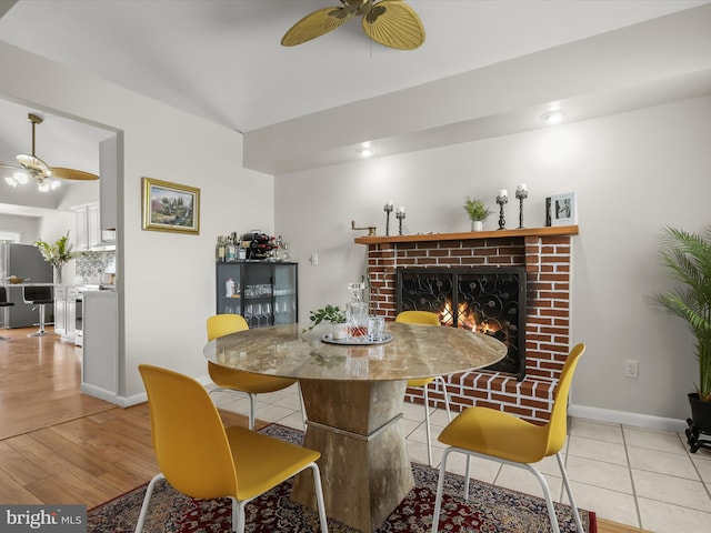 dining area with a ceiling fan, a brick fireplace, baseboards, and wood finished floors
